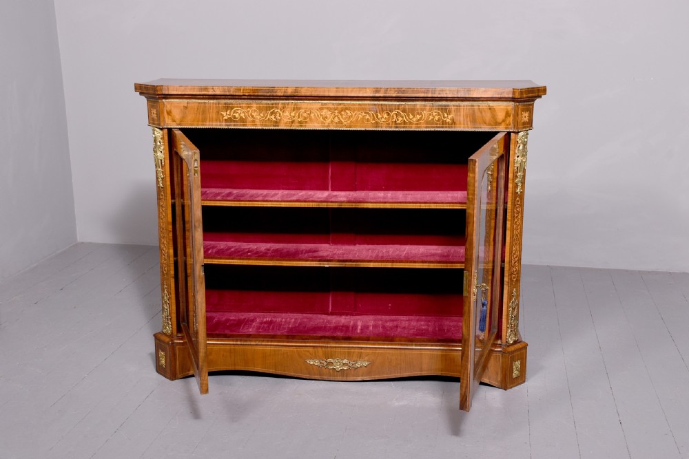 A Victorian figured walnut cabinet featuring twin glazed doors, intricate marquetry floral inlay along the frieze, gilt bronze mounts, and a red fabric-lined interior with three shelves. View IX