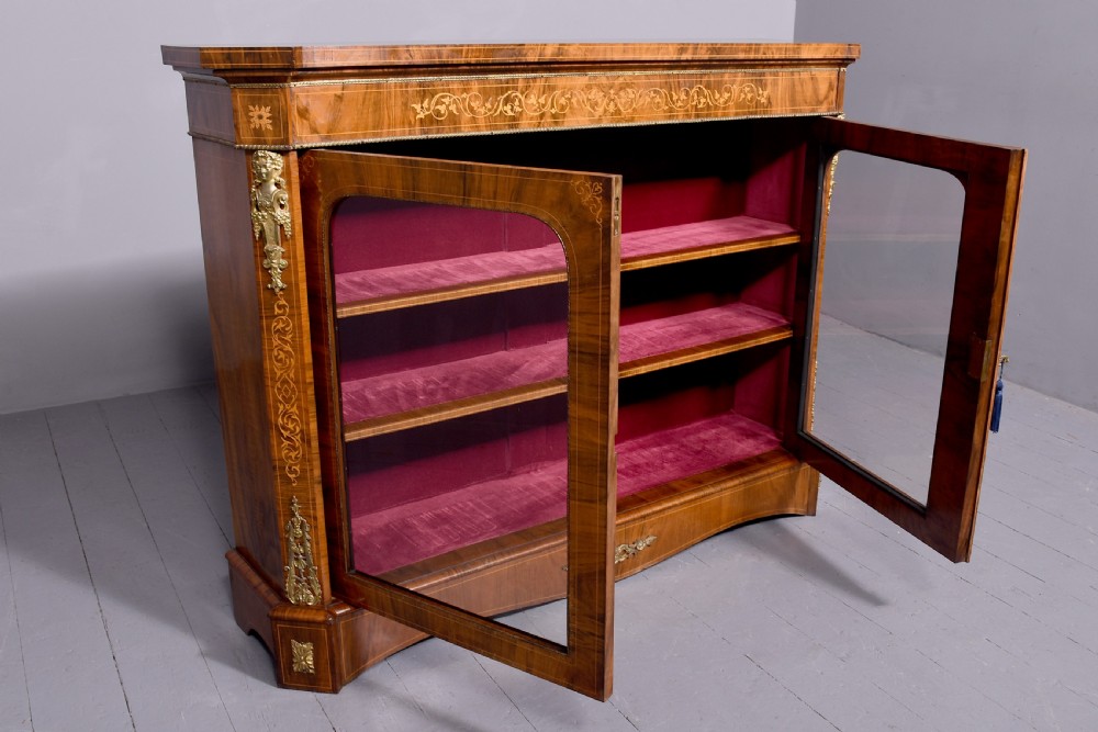 A Victorian figured walnut cabinet featuring twin glazed doors, intricate marquetry floral inlay along the frieze, gilt bronze mounts, and a red fabric-lined interior with three shelves. View X
