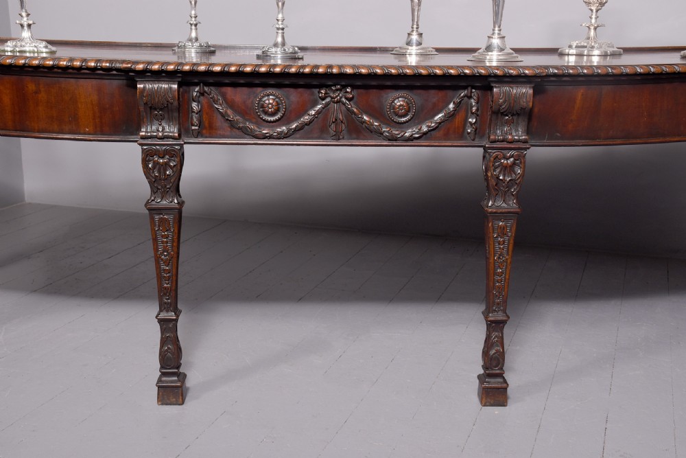 A wide George III dark mahogany serving table supported by six carved legs with intricate drapery swags running across the front frieze. View III