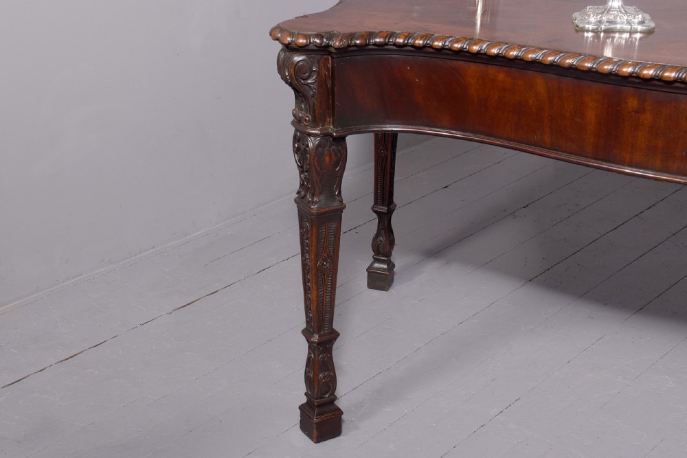 A wide George III dark mahogany serving table supported by six carved legs with intricate drapery swags running across the front frieze. View IV