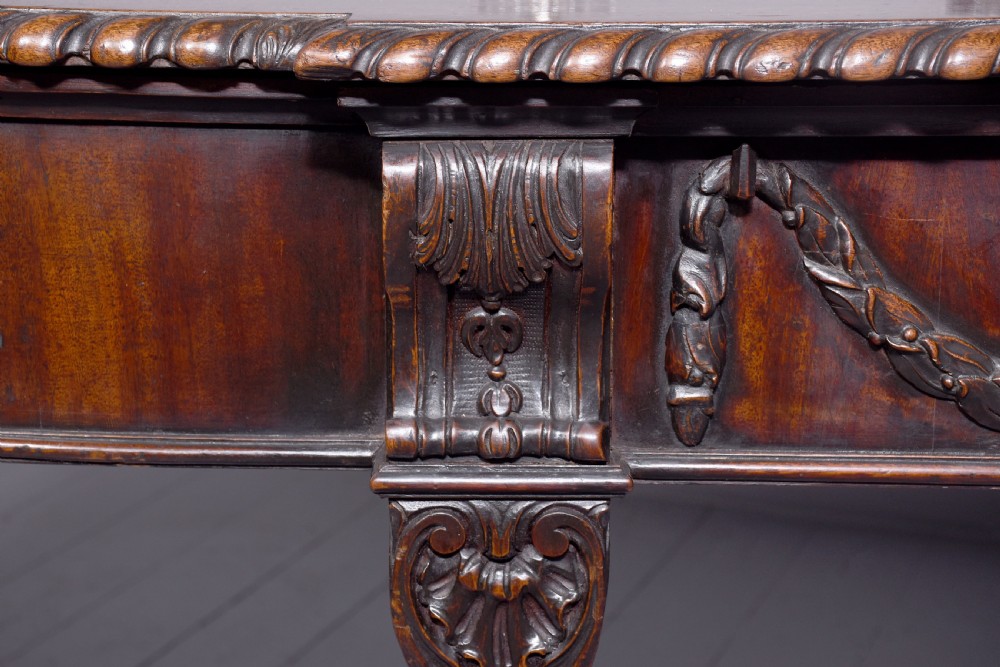 A wide George III dark mahogany serving table supported by six carved legs with intricate drapery swags running across the front frieze. View VII