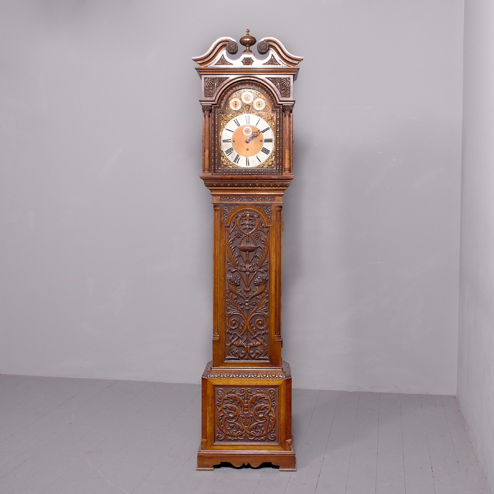 A late Victorian tall carved oak grandfather clock with a swan-neck pediment, arched brass dial, and extensive foliate relief carvings on the body and base.