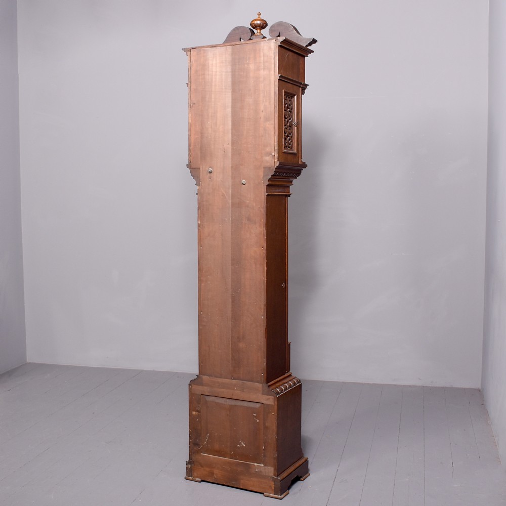 A late Victorian tall carved oak grandfather clock with a swan-neck pediment, arched brass dial, and extensive foliate relief carvings on the body and base. View II