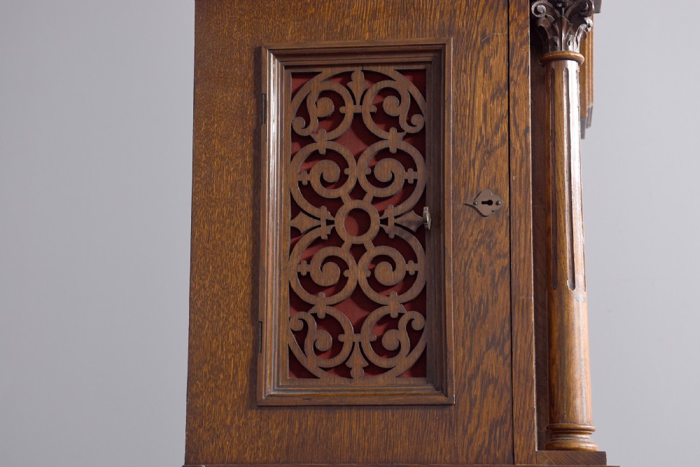 A late Victorian tall carved oak grandfather clock with a swan-neck pediment, arched brass dial, and extensive foliate relief carvings on the body and base. View III