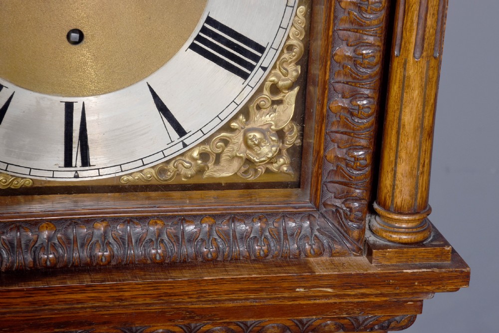 A late Victorian tall carved oak grandfather clock with a swan-neck pediment, arched brass dial, and extensive foliate relief carvings on the body and base. View IV