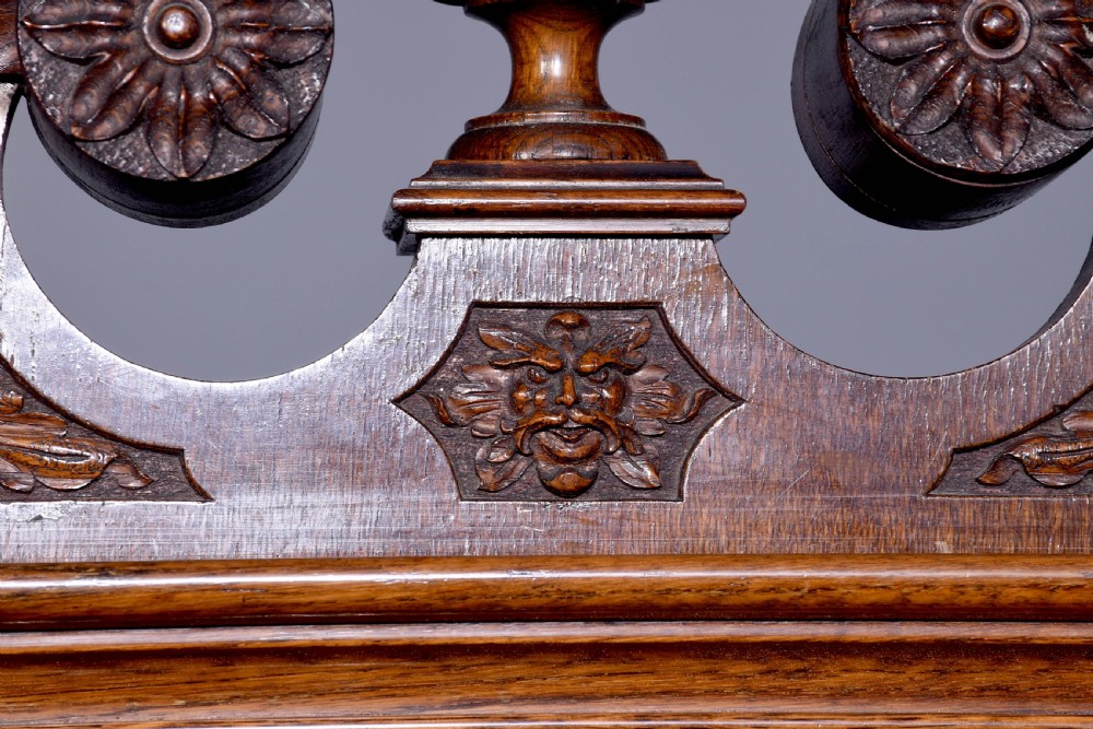 A late Victorian tall carved oak grandfather clock with a swan-neck pediment, arched brass dial, and extensive foliate relief carvings on the body and base. View VII