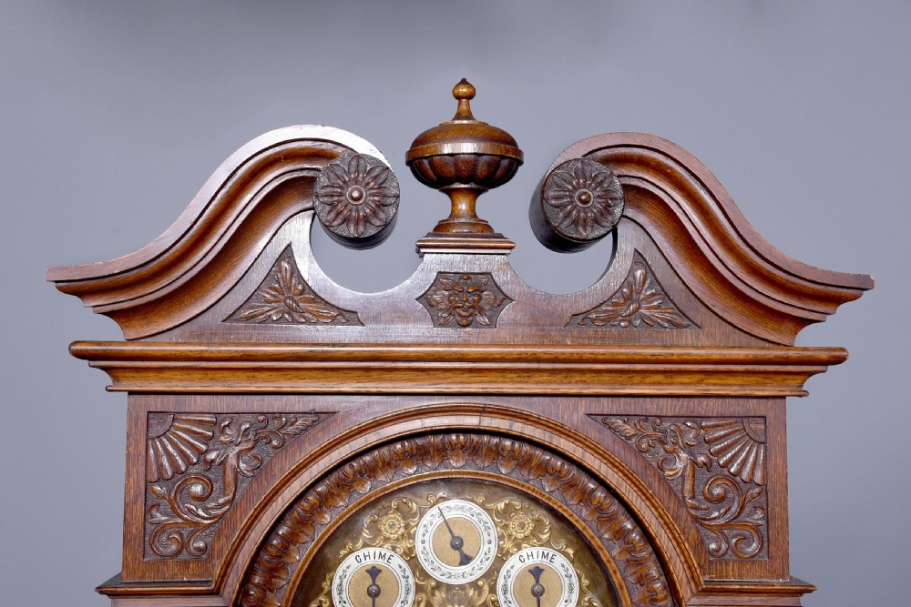A late Victorian tall carved oak grandfather clock with a swan-neck pediment, arched brass dial, and extensive foliate relief carvings on the body and base. View VIII