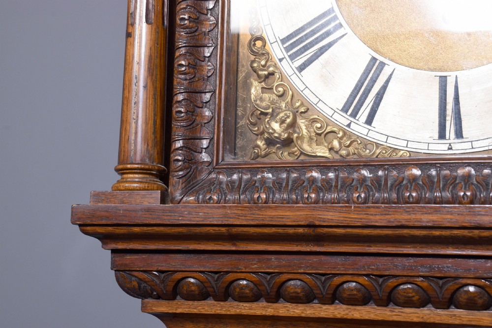 A late Victorian tall carved oak grandfather clock with a swan-neck pediment, arched brass dial, and extensive foliate relief carvings on the body and base. View IX
