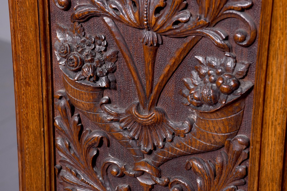 A late Victorian tall carved oak grandfather clock with a swan-neck pediment, arched brass dial, and extensive foliate relief carvings on the body and base. View XI