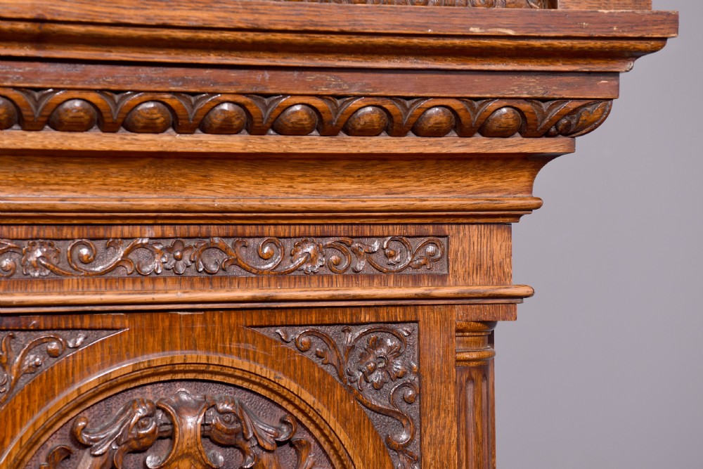 A late Victorian tall carved oak grandfather clock with a swan-neck pediment, arched brass dial, and extensive foliate relief carvings on the body and base. View XII
