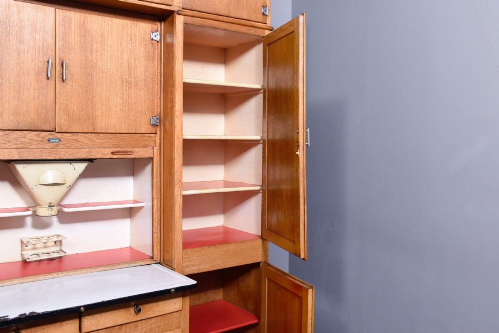 A tall oak Easiwork kitchen cabinet featuring multiple storage cupboards, drawers, an integrated enamel work surface, and an internal flour sifter mechanism. View VI