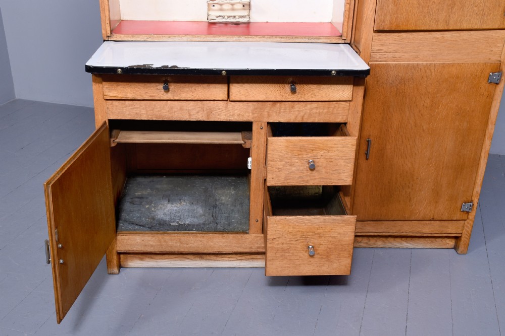 A tall oak Easiwork kitchen cabinet featuring multiple storage cupboards, drawers, an integrated enamel work surface, and an internal flour sifter mechanism. View VII