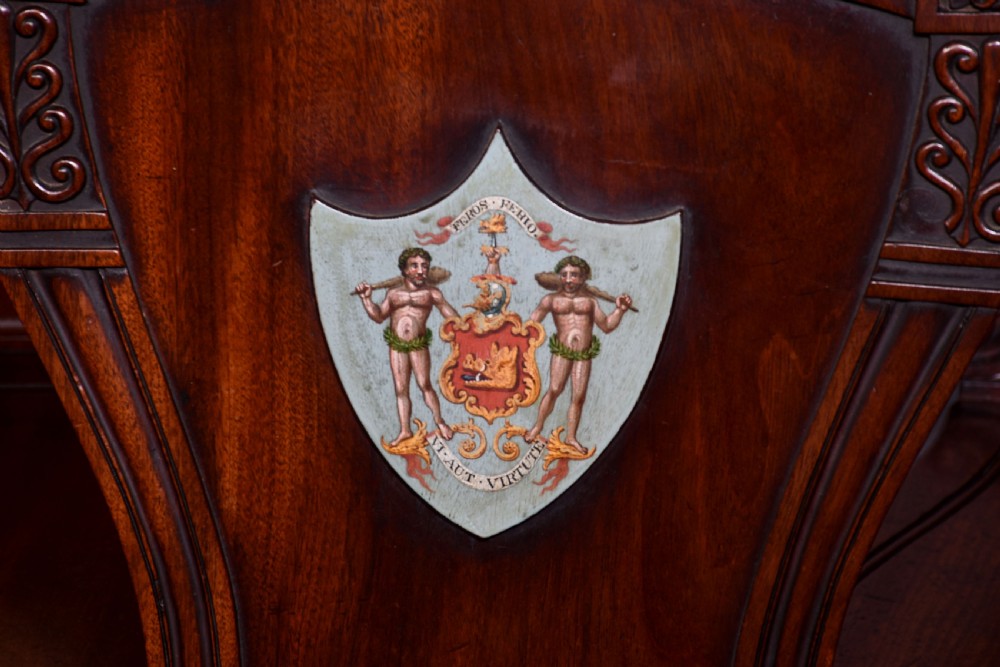 A set of five George IV mahogany hall chairs featuring carved backrest scrolls, turned fluted front legs, and hand-painted heraldic crest shields. View IV