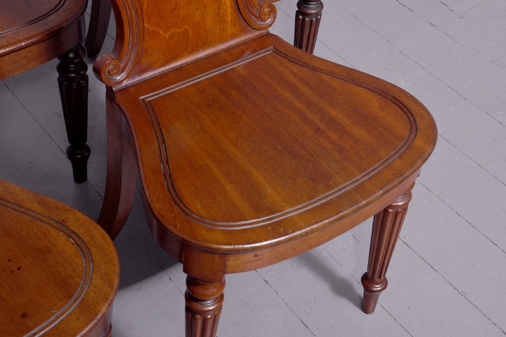 A set of five George IV mahogany hall chairs featuring carved backrest scrolls, turned fluted front legs, and hand-painted heraldic crest shields. View V
