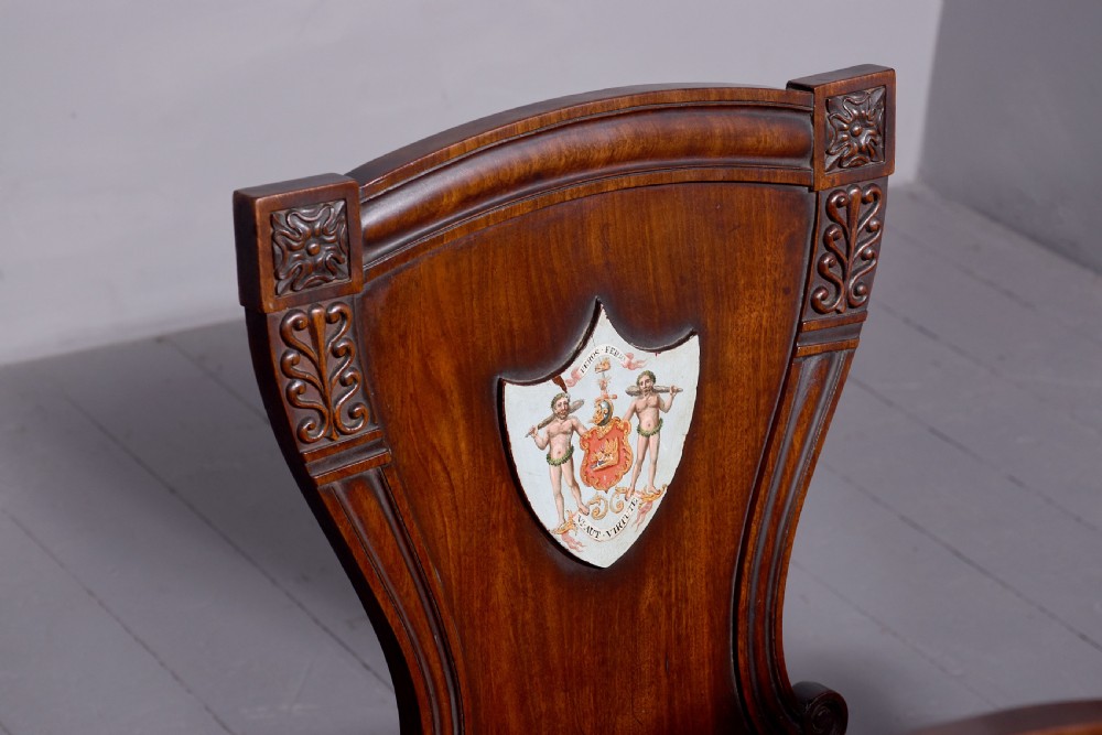 A set of five George IV mahogany hall chairs featuring carved backrest scrolls, turned fluted front legs, and hand-painted heraldic crest shields. View VI