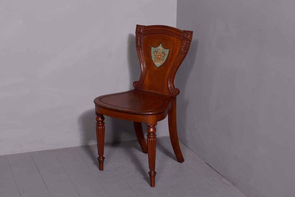 A set of five George IV mahogany hall chairs featuring carved backrest scrolls, turned fluted front legs, and hand-painted heraldic crest shields. View VIII