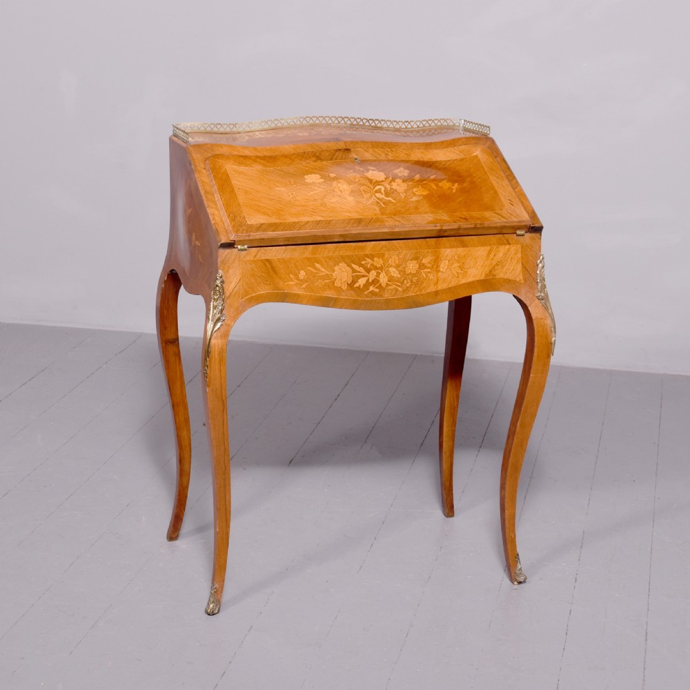A small French Louis XV style slope-front writing desk featuring floral marquetry inlays, cabriole legs with brass mounts, and a brass gallery rail.