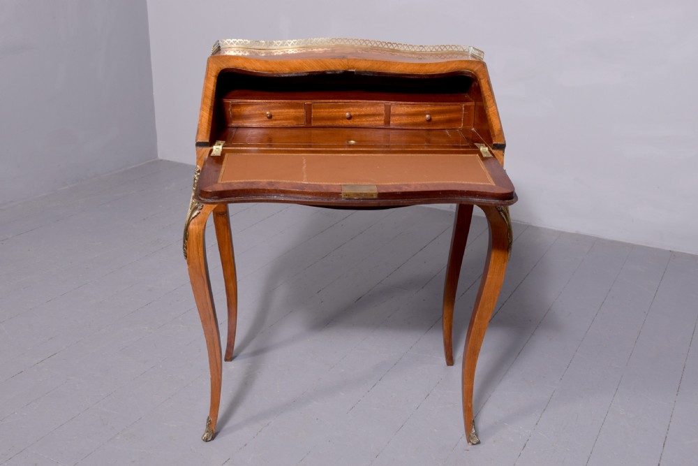 A small French Louis XV style slope-front writing desk featuring floral marquetry inlays, cabriole legs with brass mounts, and a brass gallery rail. View XV