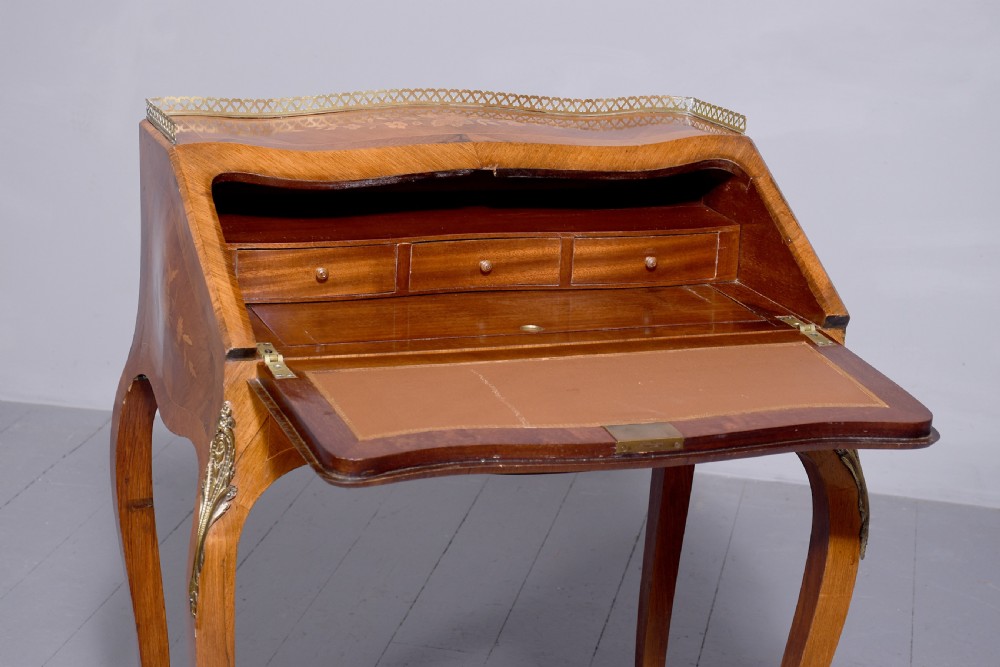 A small French Louis XV style slope-front writing desk featuring floral marquetry inlays, cabriole legs with brass mounts, and a brass gallery rail. View XVI