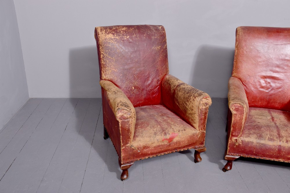 A pair of deep red leather library armchairs with high backs, rolled arms, brass stud trimming, and turned wooden front legs on castors. View II