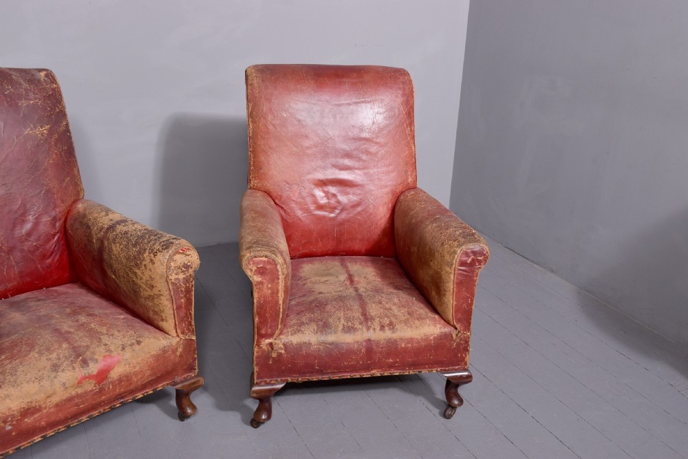 A pair of deep red leather library armchairs with high backs, rolled arms, brass stud trimming, and turned wooden front legs on castors. View III