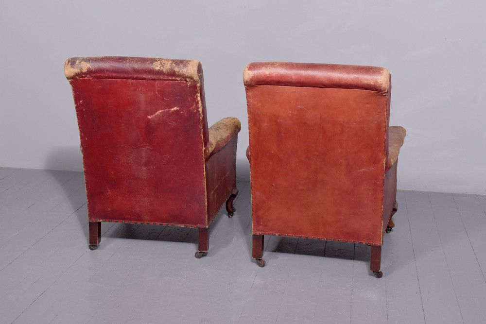 A pair of deep red leather library armchairs with high backs, rolled arms, brass stud trimming, and turned wooden front legs on castors. View IV