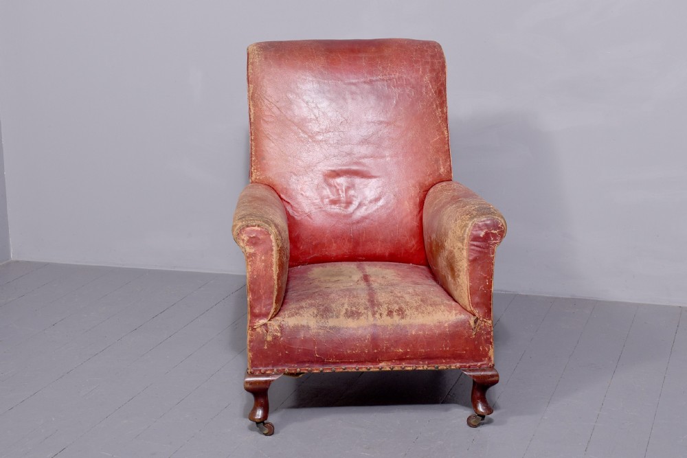 A pair of deep red leather library armchairs with high backs, rolled arms, brass stud trimming, and turned wooden front legs on castors. View V