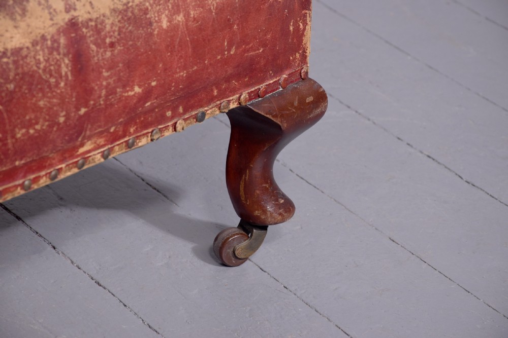 A pair of deep red leather library armchairs with high backs, rolled arms, brass stud trimming, and turned wooden front legs on castors. View VII