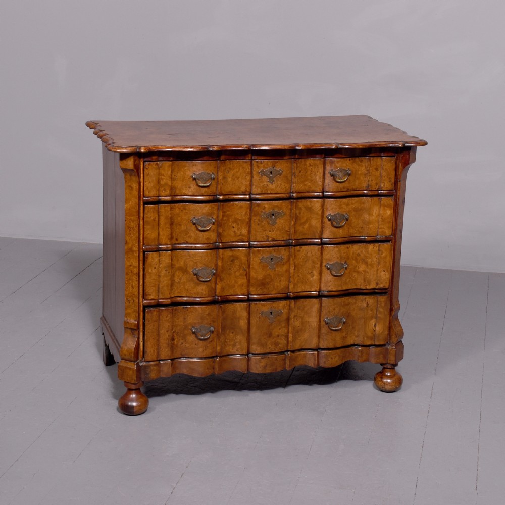 An eighteenth-century Dutch burr elm chest of drawers featuring a contoured front, four long drawers with brass drop handles, and turned bun feet.