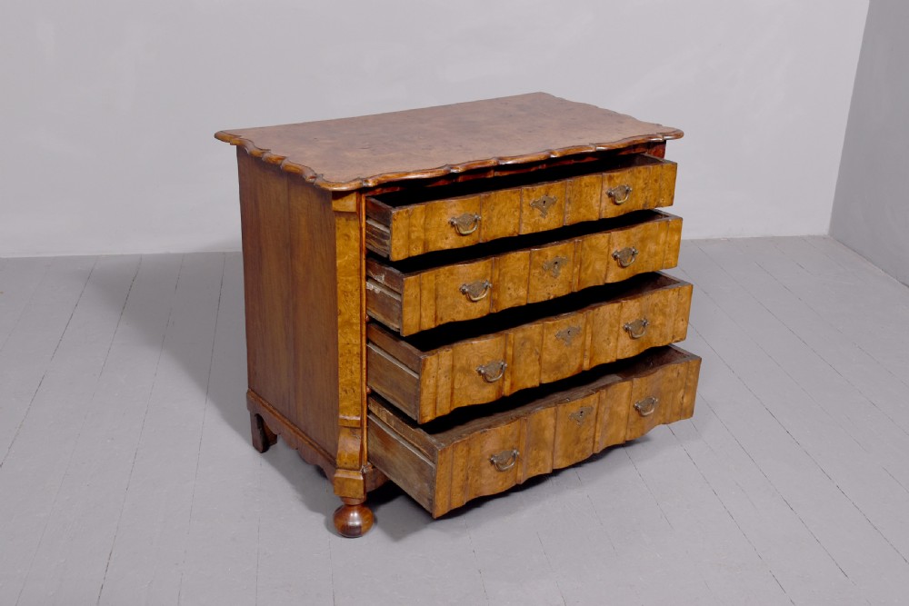 An eighteenth-century Dutch burr elm chest of drawers featuring a contoured front, four long drawers with brass drop handles, and turned bun feet. View VI