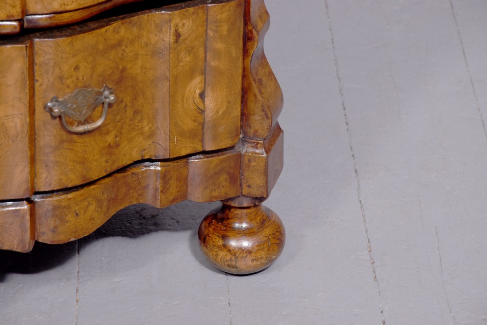 An eighteenth-century Dutch burr elm chest of drawers featuring a contoured front, four long drawers with brass drop handles, and turned bun feet. View VIII
