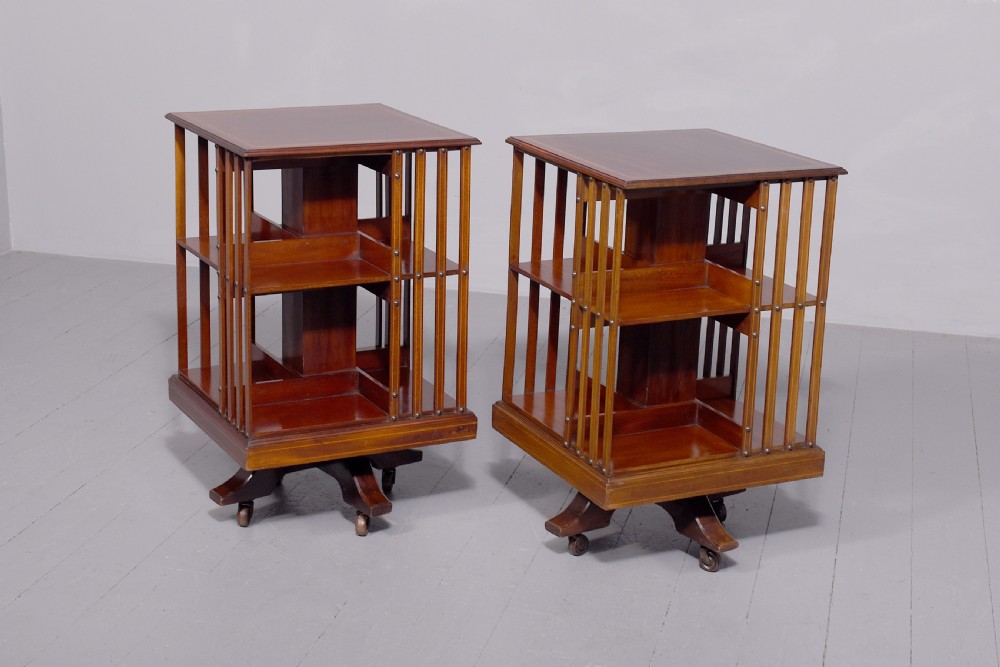 A pair of square Edwardian mahogany revolving bookcases featuring satinwood line inlay, open vertical slatted sides, two shelf tiers, and quadform bases on brass castors. View II