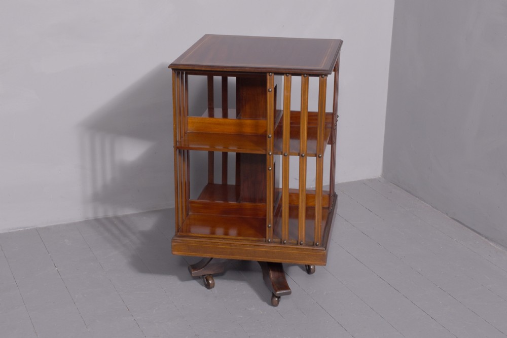 A pair of square Edwardian mahogany revolving bookcases featuring satinwood line inlay, open vertical slatted sides, two shelf tiers, and quadform bases on brass castors. View V