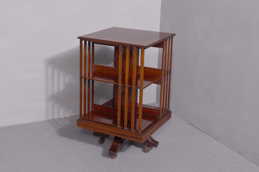 A pair of square Edwardian mahogany revolving bookcases featuring satinwood line inlay, open vertical slatted sides, two shelf tiers, and quadform bases on brass castors. View VI