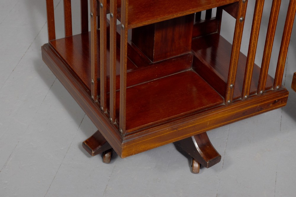 A pair of square Edwardian mahogany revolving bookcases featuring satinwood line inlay, open vertical slatted sides, two shelf tiers, and quadform bases on brass castors. View VII