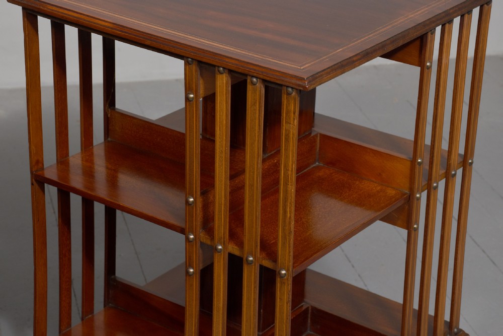 A pair of square Edwardian mahogany revolving bookcases featuring satinwood line inlay, open vertical slatted sides, two shelf tiers, and quadform bases on brass castors. View VIII