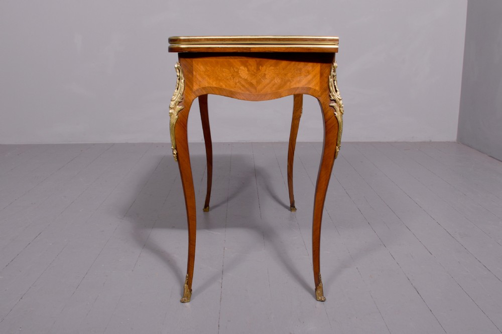 A Louis XV style French fold-over card table featuring warm brown veneer with floral marquetry inlay, cabriole legs, and gilt-bronze mounts. View II