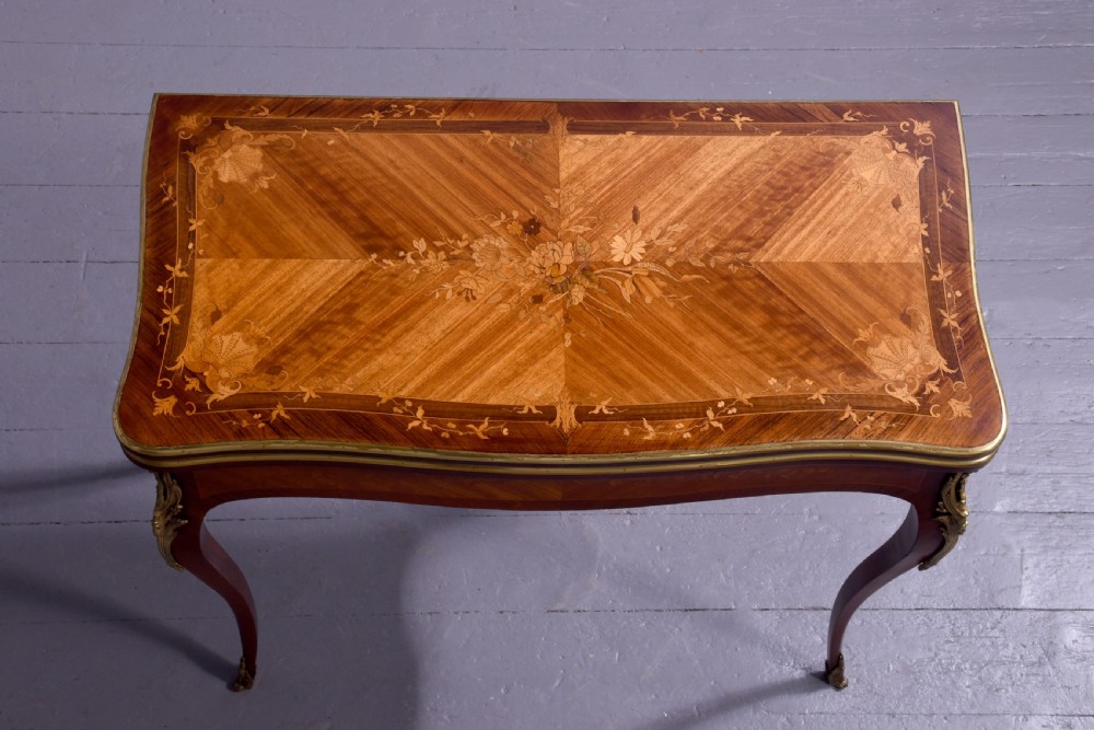 A Louis XV style French fold-over card table featuring warm brown veneer with floral marquetry inlay, cabriole legs, and gilt-bronze mounts. View IV