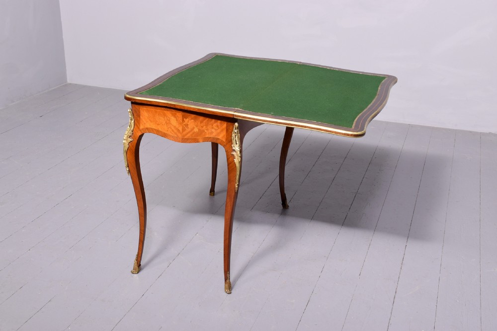 A Louis XV style French fold-over card table featuring warm brown veneer with floral marquetry inlay, cabriole legs, and gilt-bronze mounts. View V