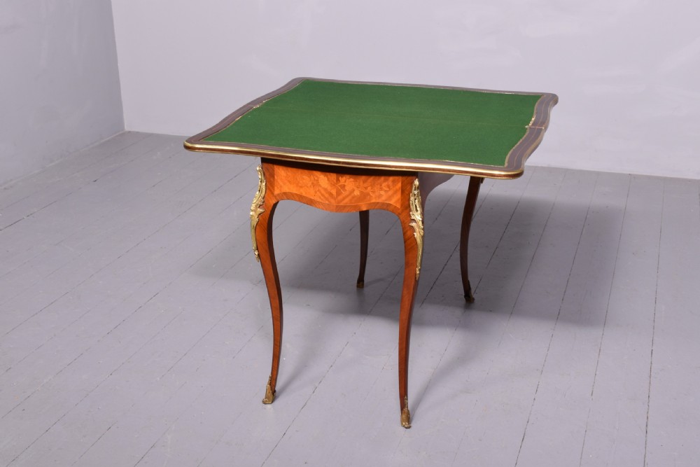 A Louis XV style French fold-over card table featuring warm brown veneer with floral marquetry inlay, cabriole legs, and gilt-bronze mounts. View VI