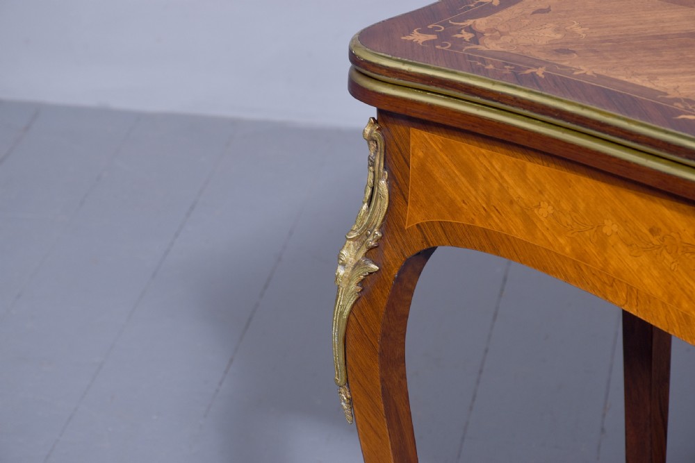 A Louis XV style French fold-over card table featuring warm brown veneer with floral marquetry inlay, cabriole legs, and gilt-bronze mounts. View X