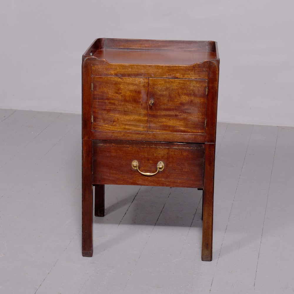 A George III mahogany tray top bedside commode featuring a raised gallery with handles, two cupboard doors, and a lower drawer with a brass bail handle.