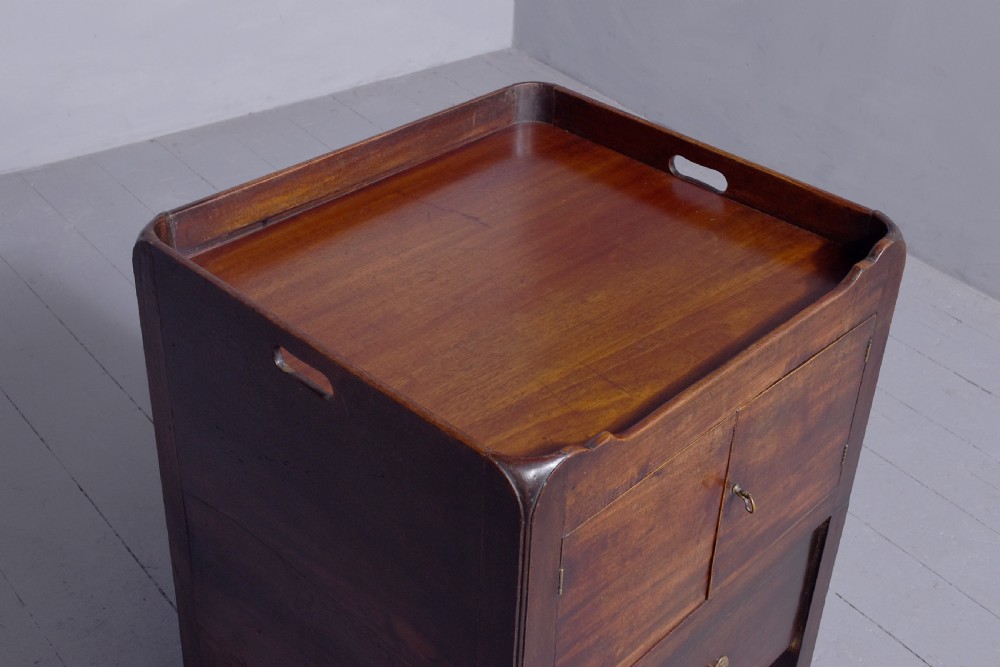 A George III mahogany tray top bedside commode featuring a raised gallery with handles, two cupboard doors, and a lower drawer with a brass bail handle. View V