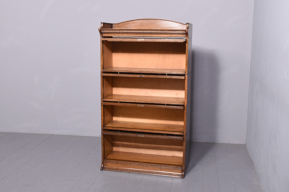 A four-tier Edwardian oak sectional bookcase featuring glazed up-and-over doors, brass handles, and an arched gallery top rail. View II