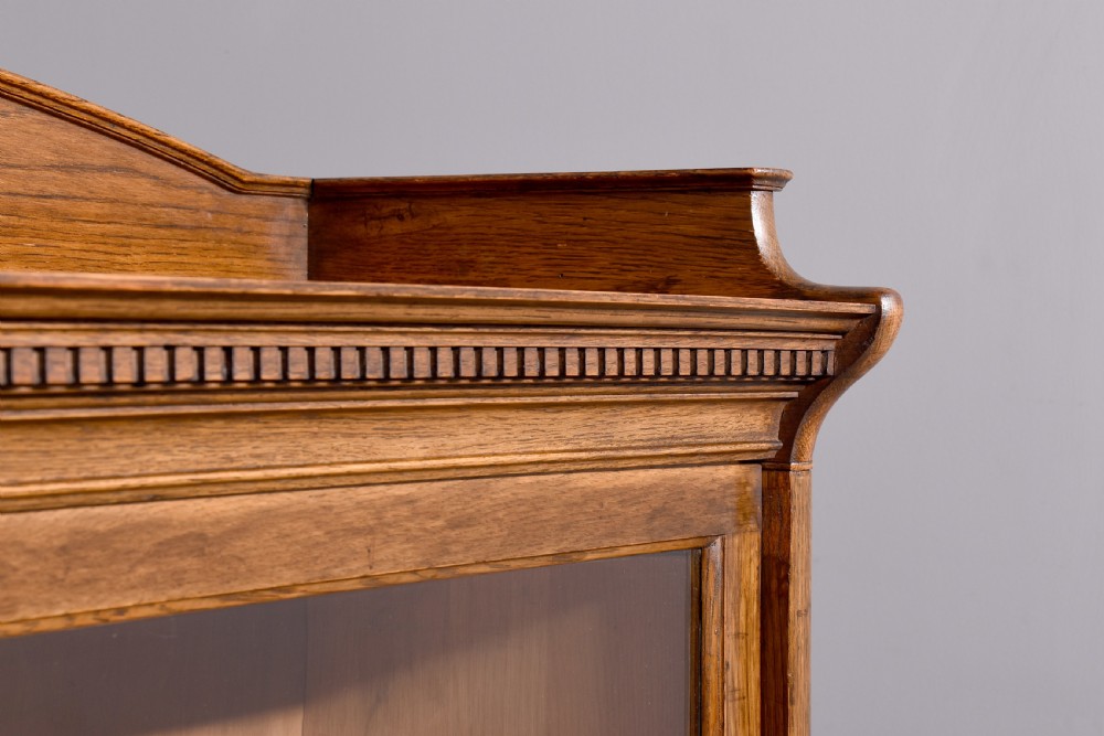 A four-tier Edwardian oak sectional bookcase featuring glazed up-and-over doors, brass handles, and an arched gallery top rail. View V
