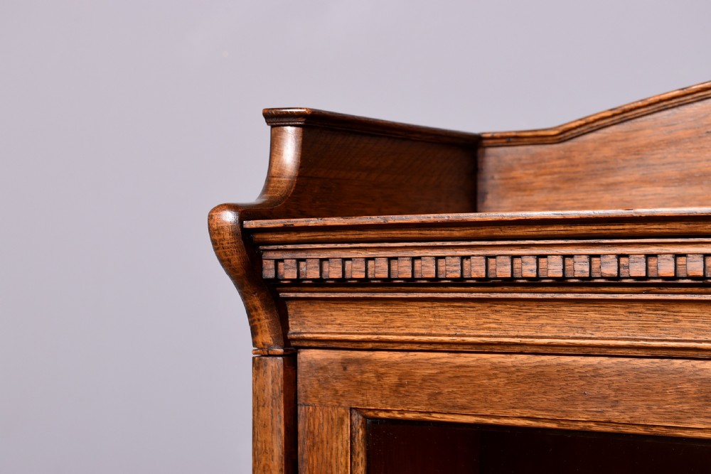 A four-tier Edwardian oak sectional bookcase featuring glazed up-and-over doors, brass handles, and an arched gallery top rail. View VII