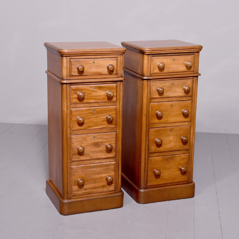 A pair of tall Victorian mahogany Wellington-style chests, each featuring five stacked drawers with turned wood knobs and stepped plinth bases.