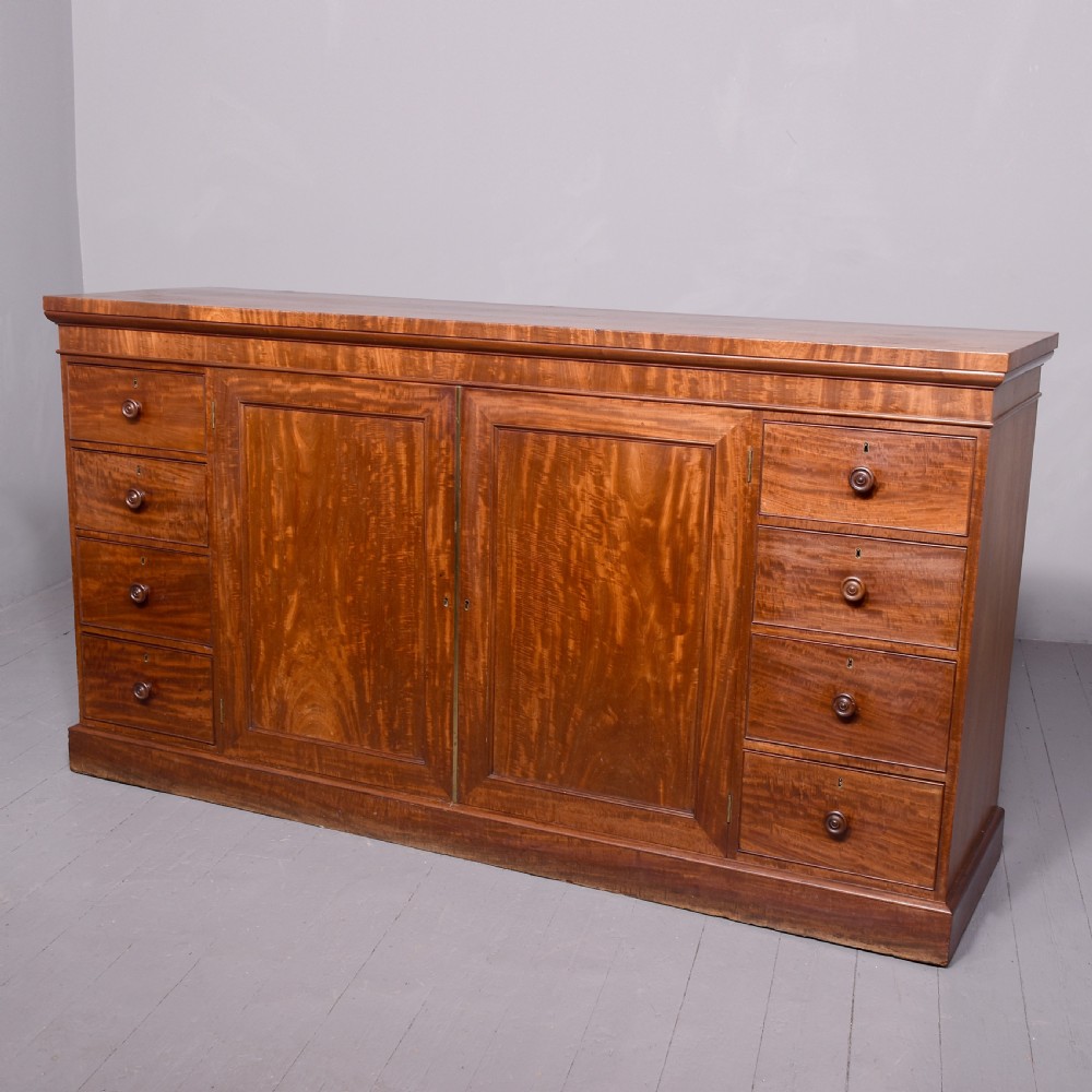 A nineteenth-century mahogany low linen press featuring two central panelled doors flanked by four drawers on each side, set on a solid plinth base.