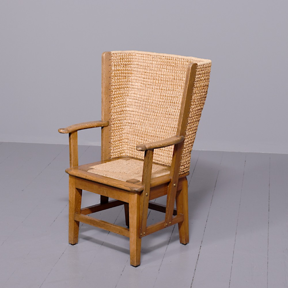 An oak armchair featuring a tall woven straw backrest, flat open armrests, and a rush seat.