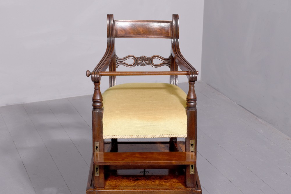 A George III mahogany childs high chair with a gold upholstered seat, safety bar, and footrest, resting atop a matching wooden stand. View II